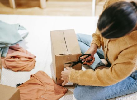 Woman carefully packs clothes into a box with scissors for shipment indoors.